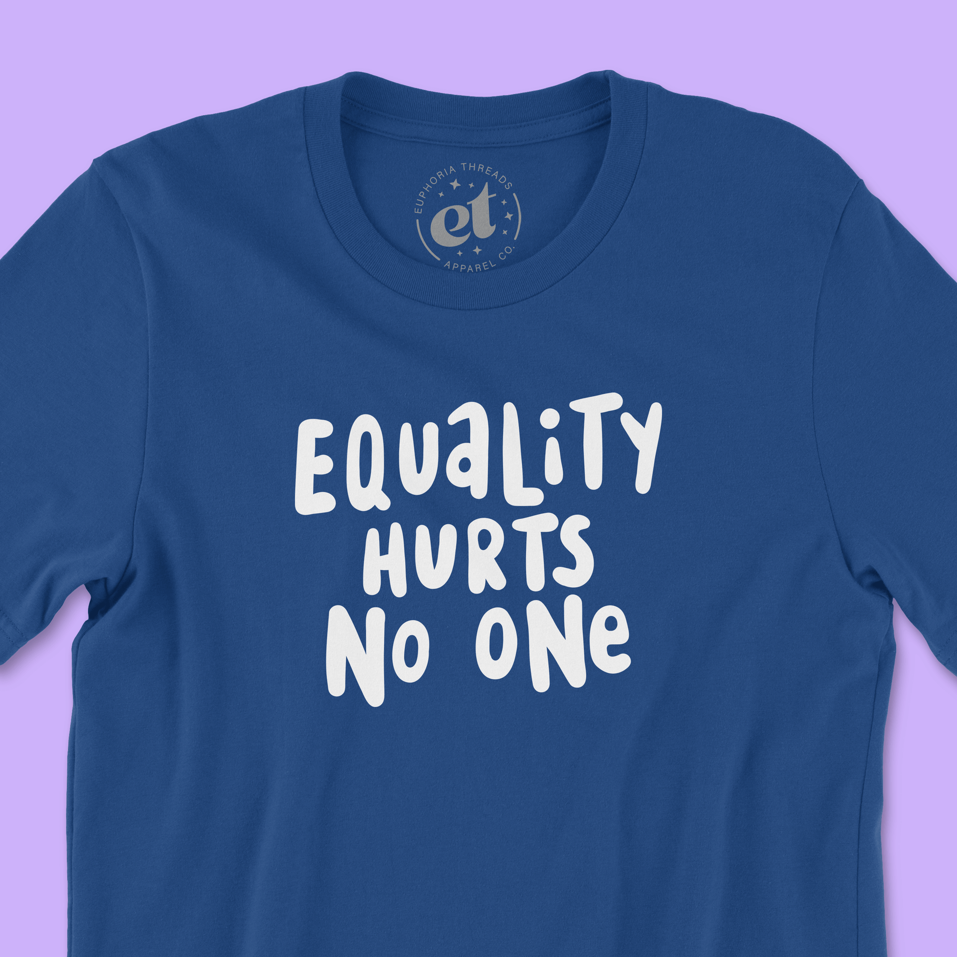Closeup of royal blue unisex 100% cotton LGBTQ pride tee with white text that says “Equality Hurts No One” in a bold, hand-lettered font. Background is light purple.
