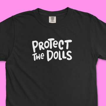 Closeup of black Comfort Colors trans rights shirt with hand written text that says "Protect the Dolls" in white.