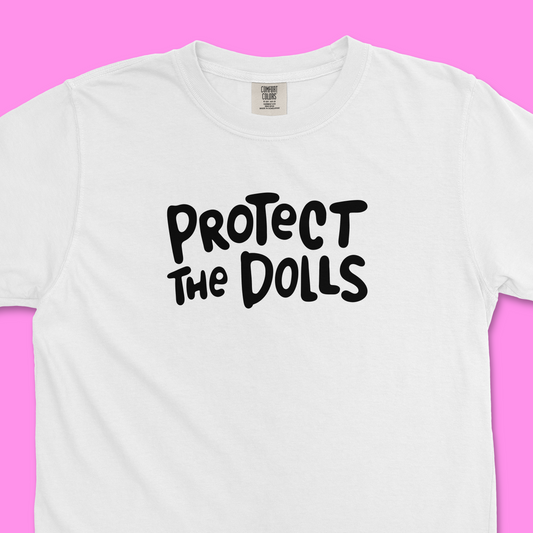 Closeup of white Comfort Colors trans rights shirt with hand written text that says "Protect the Dolls" in black.